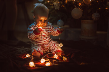 Cute little baby toddler near the Christmas tree playing with a garland and toys. The concept of the new year and Christmas mood