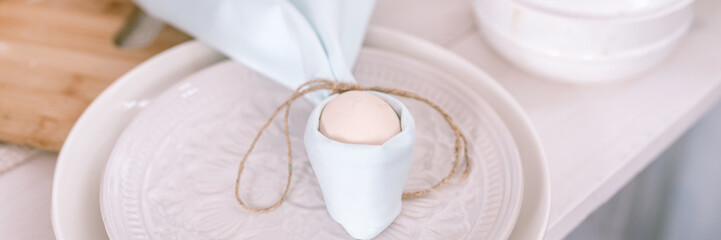 happy easter holiday in springtime season. festive home decor. traditional food. white beige chicken egg wrapped in a pale blue cloth like rabbit or bunny ears in a plate on the table. banner