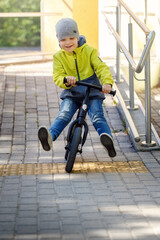 Happy cute boy wear yellow jacket and grey cap playing balance bike exercise in the morning day.
