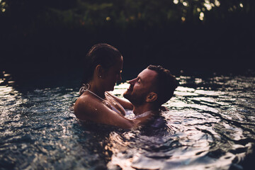Cheerful Caucaisan couple in love bonding and cuddling while swimming in pool in Indonesia, young carefree marriage 20 years old visiting Bali during summer honeymoon for recreating together
