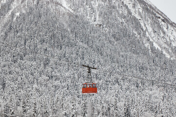 pendulum lift in mountains, cable car, red cabin, winter, snow on slopes and her on forest,