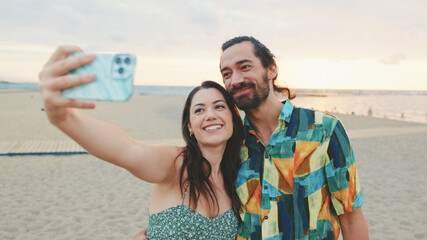 Laughing couple taking selfie on mobile phone while standing on the beach