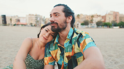 Fototapeta premium Happy couple sitting hugging on blanket on the beach