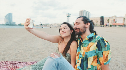 Happy couple taking selfie on mobile phone while sitting on the beach