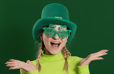 St. Patrick's Day leprechaun model girl in green hat, funny clover shaped sunglasses, isolated on...