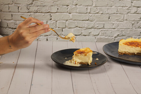 hand with a fork picking up cheesecake and slices on a white brick wall