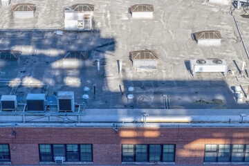 Flat rooftop of two storey red brick building showing air conditioners, skylights and plumbing vent...