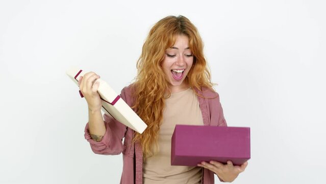 Young redhead woman surprised and holding a gift over isolated background