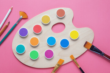 Paints, paintbrushes and palette on pink paper background. Copy space