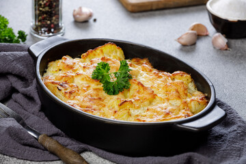 Potato casserole with cheese and parsley on stone background. French cuisine.