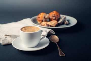 Taza de café con galletas y muffins en plato con cuchara de cobre, sobre fondo azul oscuro