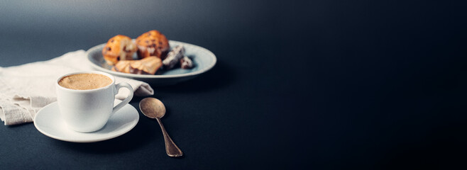 Taza de café con galletas y muffins en plato con cuchara de cobre, sobre fondo banner largo azul oscuro