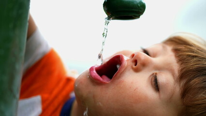 Little kid boy drink water at fountain in slow motion. Sunny summer day in city. Thirsty male child...