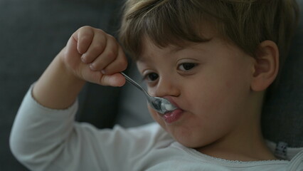 Child eating yogurt with spoon. Close up face of little boy eats nutritious breakfast food