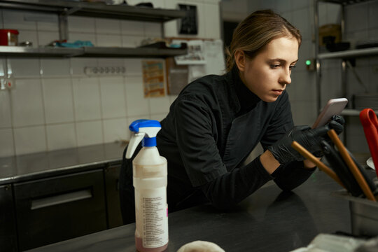 Young Kitchen Worker Is Looking At Something On Her Phone