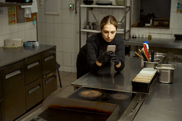 Female chef stands at the cutting table with a phone