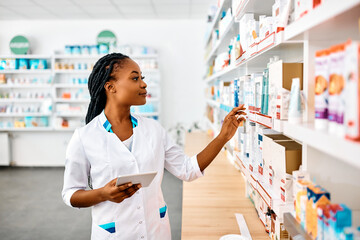 Young black pharmacist using touchpad while working in drugstore.