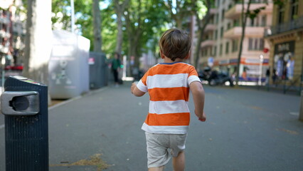 Back of little boy running in European city street outside during sunny day. Child runner in urban...