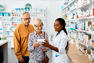 Obraz premium Young black pharmacist assists senior couple in buying medicine in drugstore.