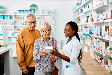 Young black pharmacist assists senior couple in buying medicine in drugstore.
