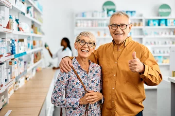 Fotobehang Happy senior man shows thumbs up while buying with his wife in pharmacy and looking at camera. © Drazen
