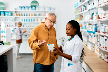 African American female pharmacist advising senior man in pharmacy.