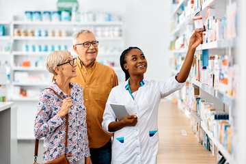 Happy African American female pharmacist assists senior couple who is buying medicine in drugstore.
