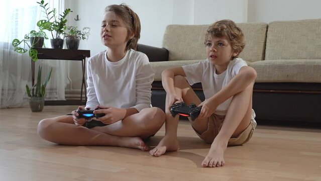 Gamer Children siblings playing video games in front of tv, using playstation joystick. Kids brother sister having fun enjoying their hobby leisure activity at home
