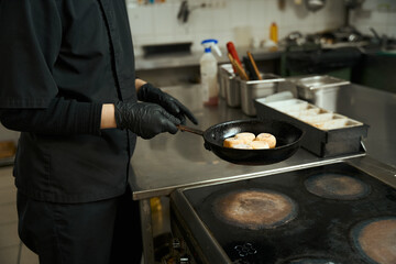 Chef fries golden cheesecakes in a pan in restaurant kitchen