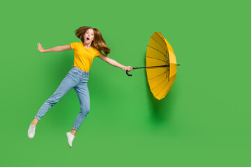 Full length portrait of speechless impressed girl jump hand hold umbrella flying isolated on green...