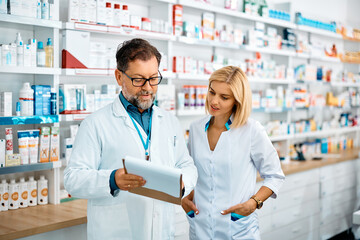 Two pharmacists cooperating while going through paperwork in pharmacy.