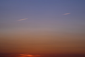 Fototapeta na wymiar Two airplanes traces at the sunset sky, one chasing another