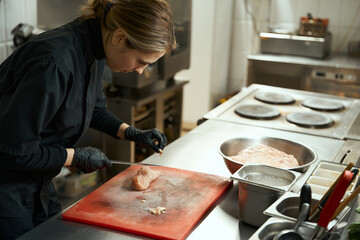 Female chef cleans raw chicken fillet from fat, she uses a professional knife