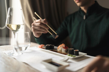 Obraz na płótnie Canvas Table filled with friends, enjoying plates of sushi rolls, sashimi, and sake, in a relaxed and casual atmosphere. woman savoring every bite of a healthy delicious sushi roll, in trendy sushi bar