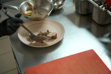 Kitchen worker puts stewed meat, mushrooms and vegetables on plate
