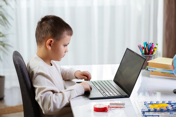 Smart little boy student programs game at home. Child using laptop, his hands typing on keyboard. Programming lesson. Side view