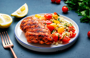 Roasted chicken breast with tabbouleh salad with bulgur, tomatoes and parsley with oil lemon dressing, green table background, top view