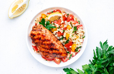 Grilled chicken breast fillet with tabbouleh salad with bulgur, tomato and parsley with lemon dressing, white table background, top view