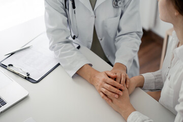 Doctor and patient sitting at the desk in clinic office. The focus is on female physician's hands reassuring woman, close up. Perfect medical service, empathy, and medicine concept