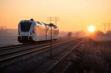 A regional commuter train in the countryside during a winter sunrise.