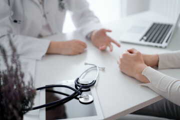 Doctor and patient sitting and discussing something at the desk in clinic. The focus is on the stethoscope lying on the table, close up. Medicine and healthcare concept