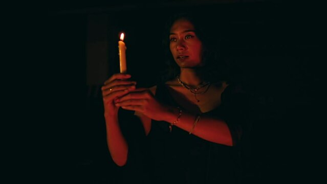 a woman performs a satanic ritual movement with a lit candle in the dark