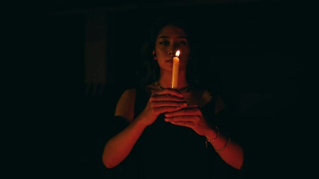 a woman performs a satanic ritual movement with a lit candle in the dark