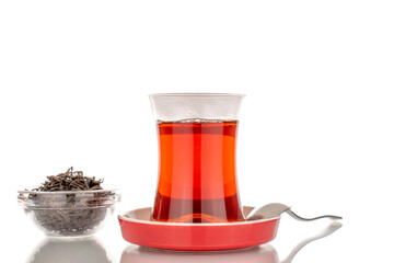 One glass of black aromatic tea with a metal spoon on a ceramic saucer, macro, isolated on white background.
