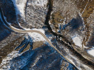 Aerial drone view on the road trough the hill and mountain in winter day covered with snow with rock and trees and river in Serbia
