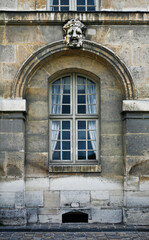 Obraz premium Paris ancient stone building facade with a French window, white curtains, stucco fretwork arch and dramatic mask, and cobblestone pavement