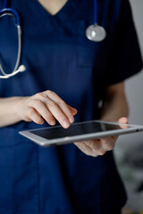 Doctor woman using tablet computer while standing near panorama window in clinic, close up. Physician or surgeon at work. Medicine concept