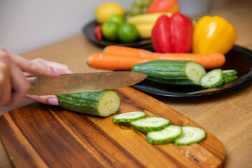 female hands slicing a cucumber on a wooden cutting board