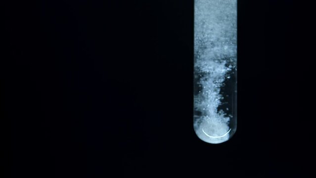 Natural fuel. Reaction in water. Boiling and fizzing of ingredients in liquid. Getting energy.  Test tube with colorless liquid on a black background. Reagent. Dissolution of component.