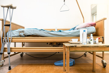 side view of homecare adjustable electric hospital bed, crutches and table with medicine at home